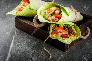 Mexican food. Healthy eating. Wrap sandwich: green lavash tortillas with spinach, fried chicken, fresh greens salad, tomatoes, yoghurt sauce. Wooden tray, dark stone table. Copy space